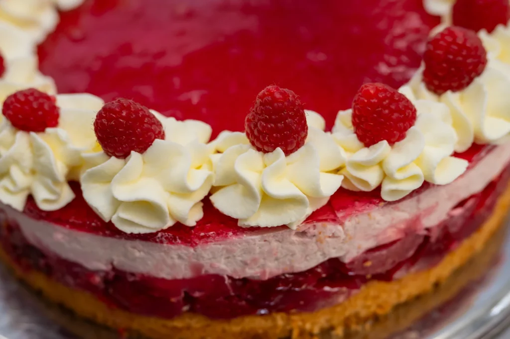 Nahaufnahme einer Torte mit rotem Guss, Sahnetupfen und Himbeeren