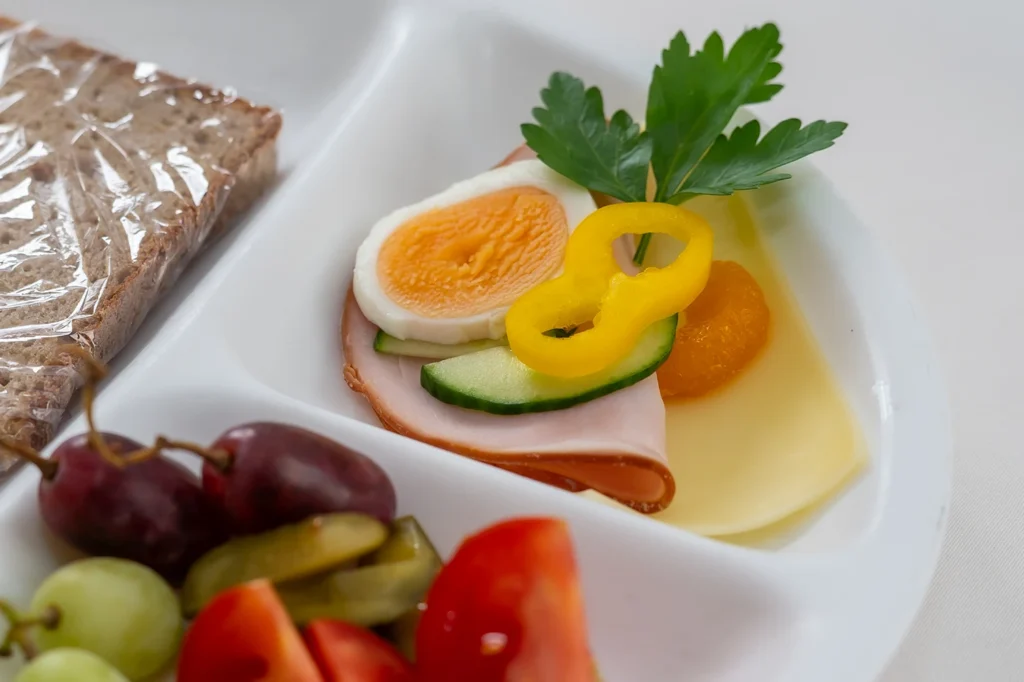 Nahaufnahme eines Abendbrottellers mit Putenbrust, halbem Ei, Paprika, Gurke, Käse, Trauben und Tomaten