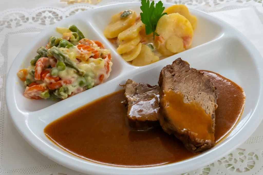Teller mit drei Fächern: Schweinebraten in brauner Soße, Kartoffelauflauf und Rahmgemüse