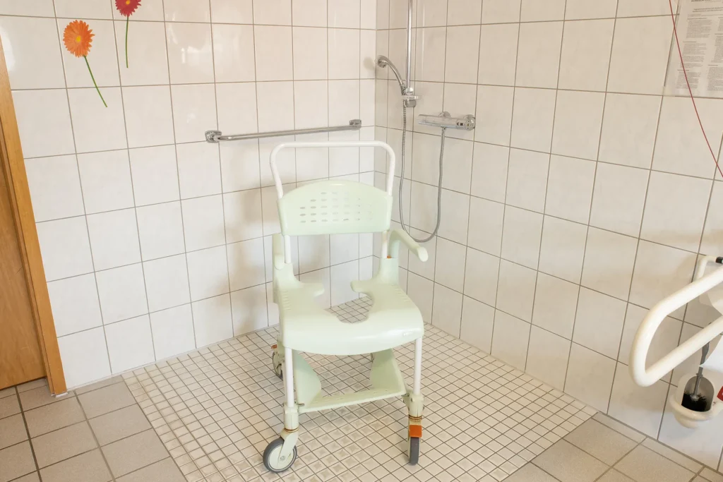 Bodengleiche Dusche im Pflegebad mit Duschrollstuhl und Haltegriffen