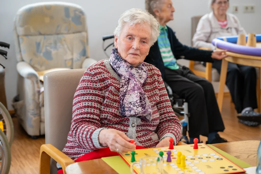 Eine Bewohnerin mit lila Halstuch zieht am Tisch eine Spielfigur auf dem Spielbrett