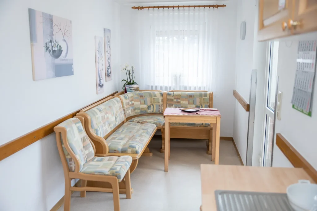 Eckbank mit Tisch an einem Fenster, an der Wand drei Blumenbilder