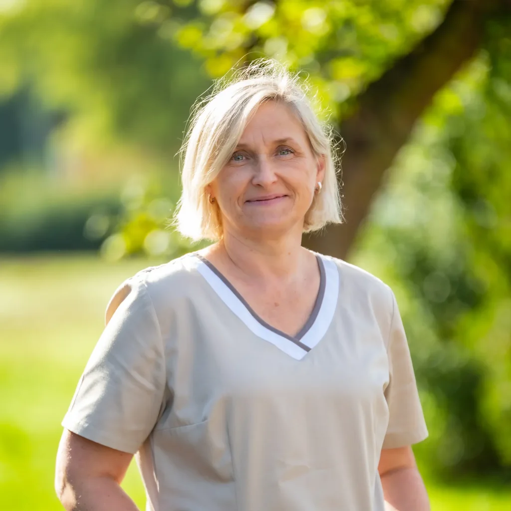 Mitarbeiterin mit blonder Kurzhaarfrisur in beigem Kasack
