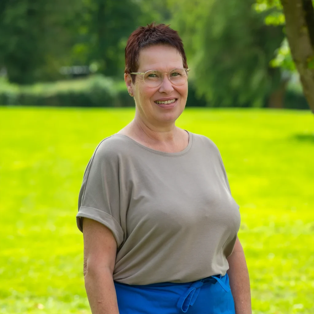 Mitarbeiterin mit kurzen dunkelroten Haaren und Brille in olivgrauem Shirt