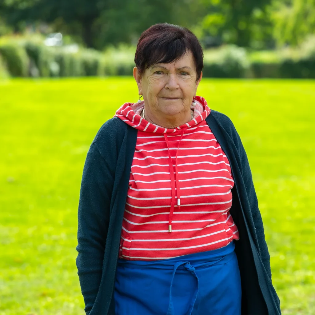 Ältere Mitarbeiterin mit kurzen dunklen Haaren in rot-weiß gestreiftem Pullover und dunkelblauer Strickjacke