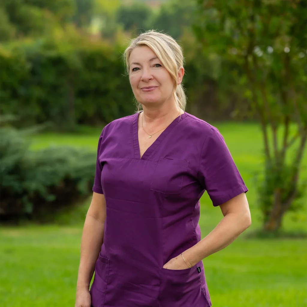 Mitarbeiterin mit blonden Haaren in violettem Kasack
