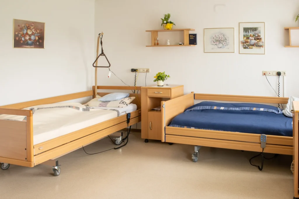 Doppelzimmer mit zwei Pflegebetten, Nachttisch und Bildern an der Wand